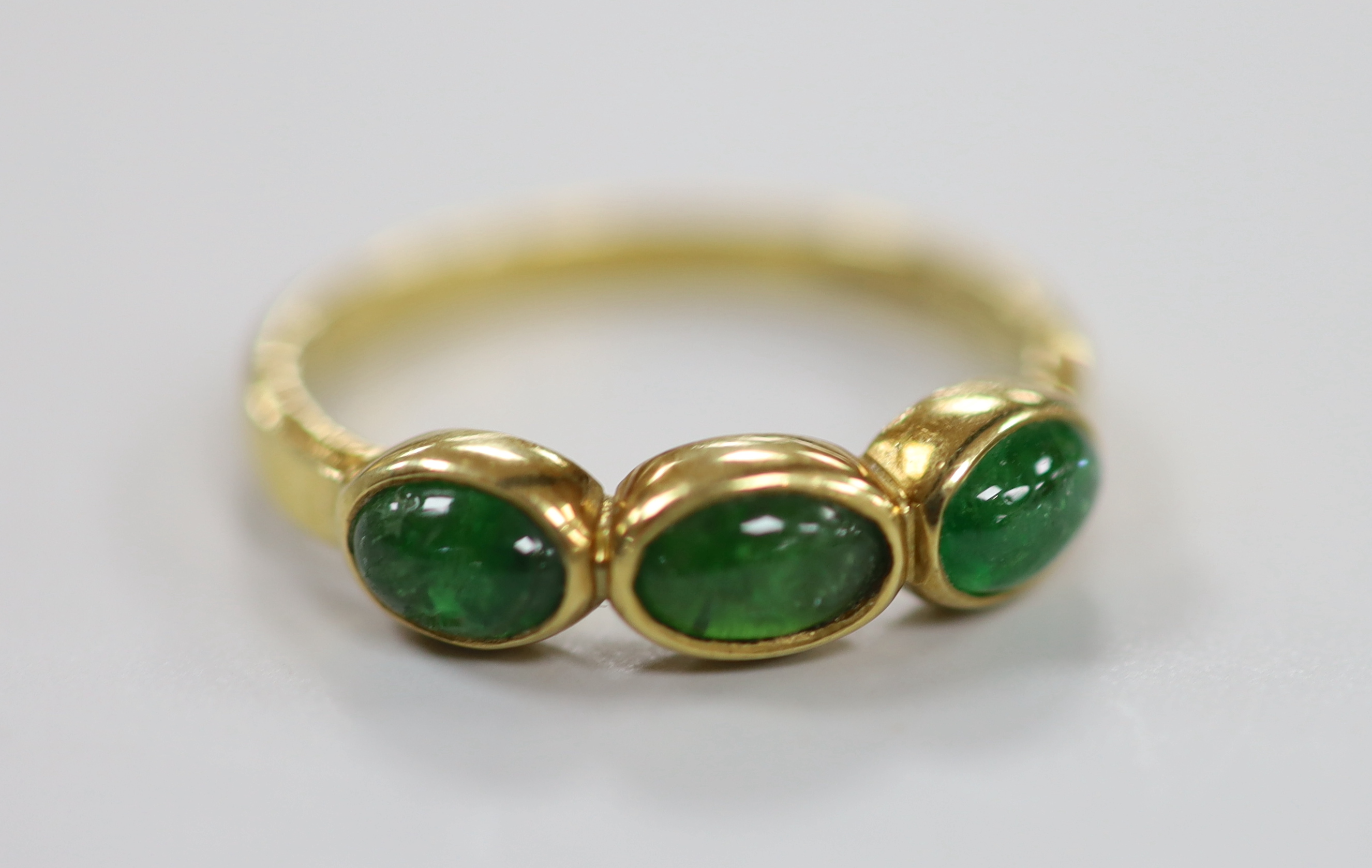 A modern 18ct gold and three stone cabochon emerald set half hoop ring, size N, gross weight 3.2 grams.